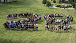 A large group of people on a grassy field standing in the form of the numbers 