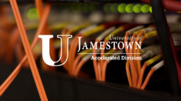 The logo of University of Jamestown Accelerated superimposed over an image of orange fiber-optic cables plugged into networking hardware.