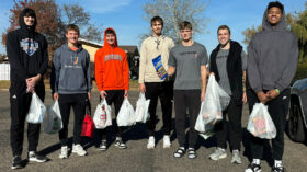 A group of men hold bags full of donated food for a food drive