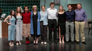 The cast of a play stands for a group portrait on stage in front of a restaurant made to look like a set.